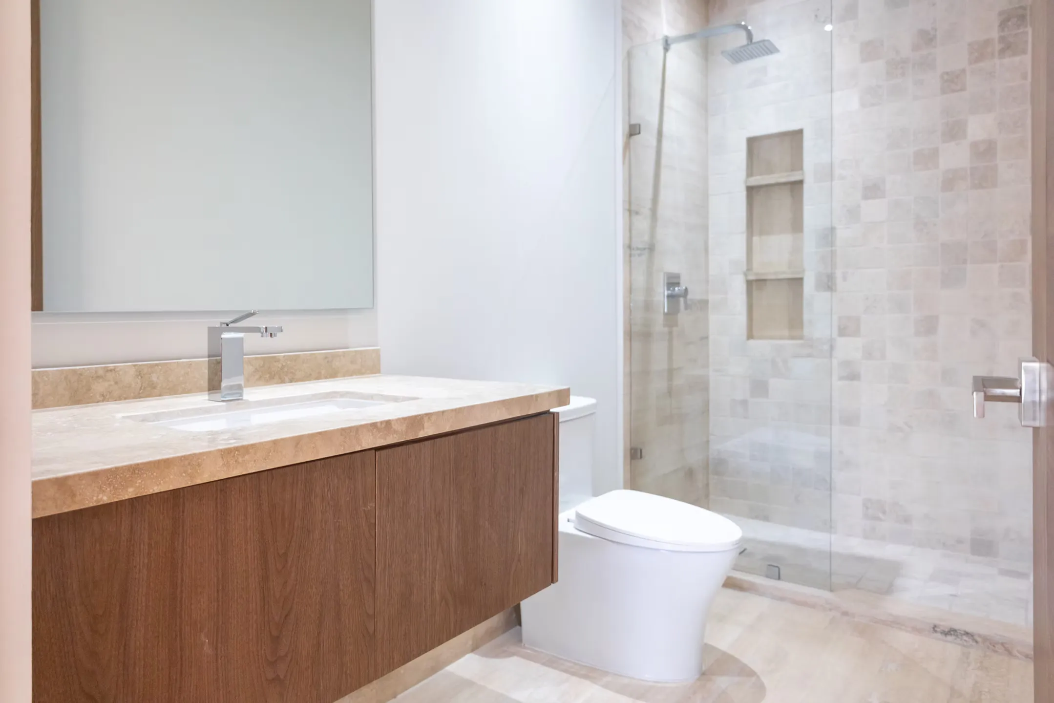 Baño remodelado con mueble de lavabo flotante en madera, cubierta de mármol, espejo amplio y regadera con cancel de vidrio y nicho empotrado